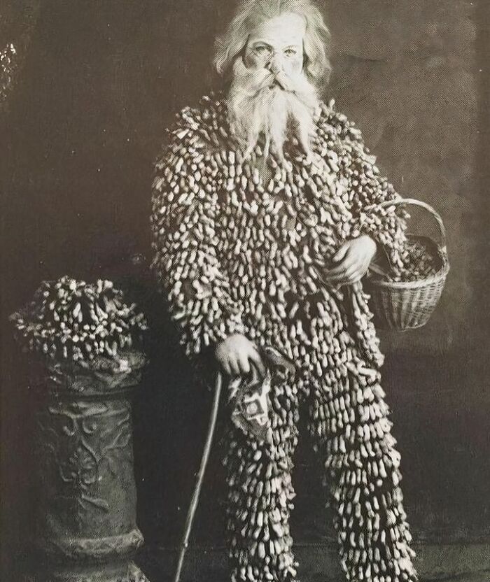 Victorian man covered in hundreds of peanuts on his clothing holding a basket and cane in a strange moment.