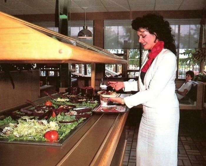 Woman serving herself salad at a vintage buffet of beloved foods and drinks that broke hearts when they disappeared