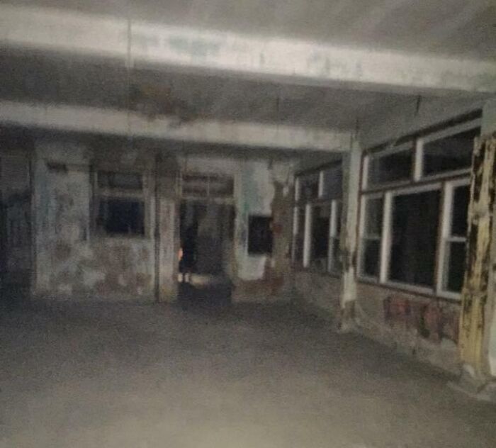 Empty dark room with peeling walls and windows, evoking chilling ghost encounters in a spooky abandoned building.