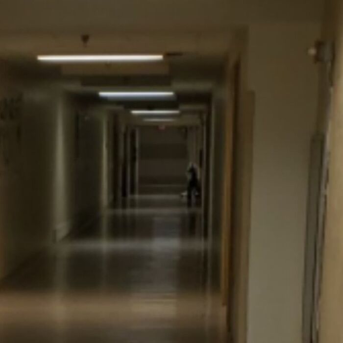 Dimly lit empty hallway with a shadowy figure sitting in the distance, evoking chilling ghost encounters atmosphere.