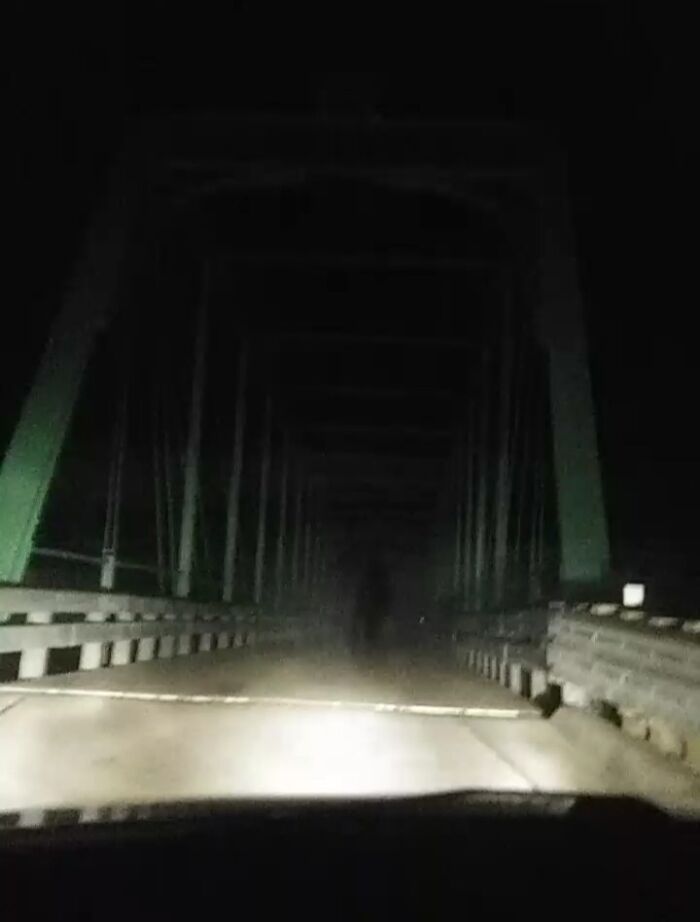 View from car headlights on a dark bridge with a faint ghostly figure, suggesting chilling ghost encounters at night.