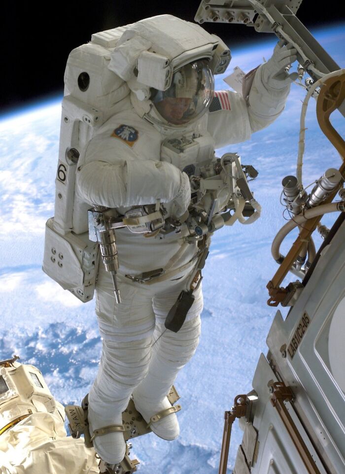 Astronaut in a space suit performing a spacewalk outside the spacecraft with Earth visible in the background.