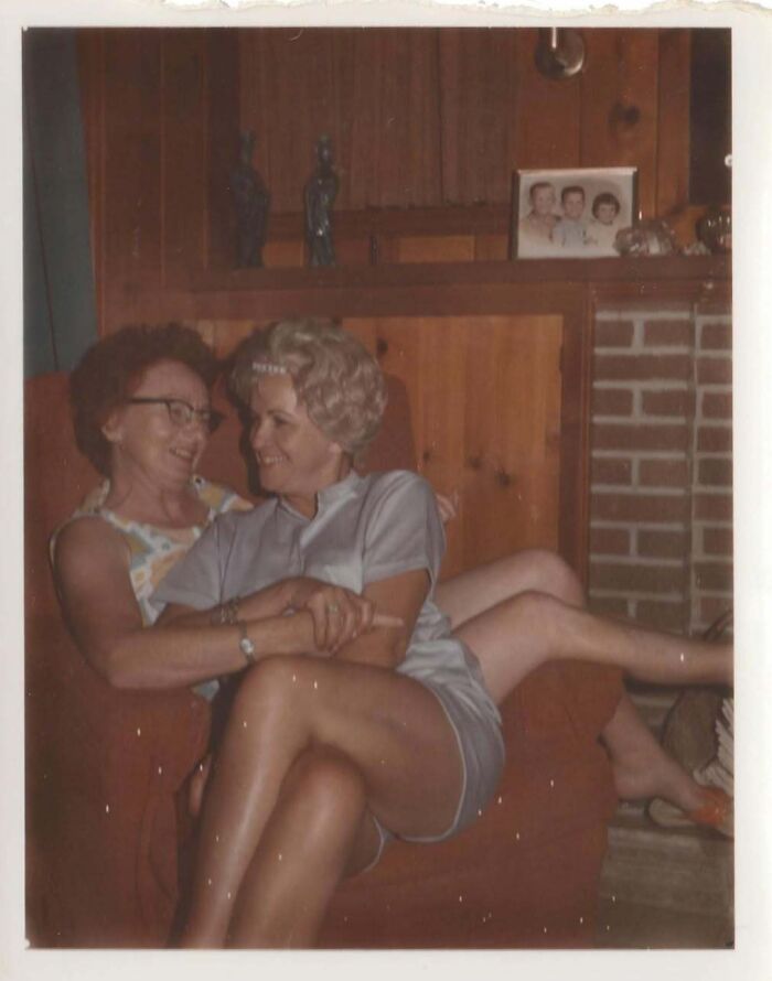 Two women sitting closely on a couch in a cozy vintage room, showcasing interesting and mesmerizing vintage photos.