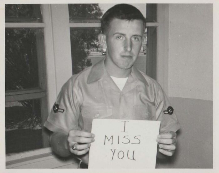 Black and white vintage photo of a young man in uniform holding a sign that says I miss you, capturing history moments.