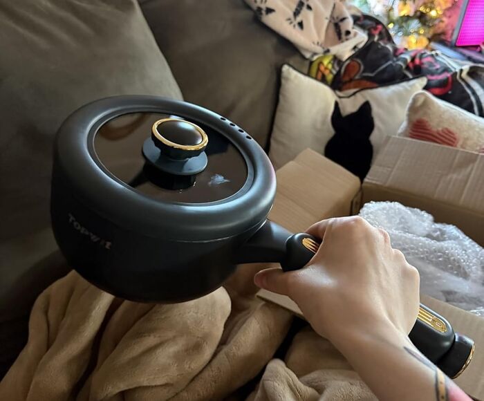 Hand holding a black kitchen gadget pot with lid, demonstrating one of the bad yet brilliant kitchen gadgets.
