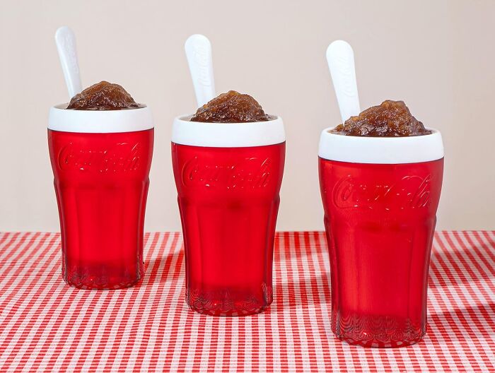 Three red Coca-Cola shaped kitchen gadgets filled with a frozen slushy dessert on a red and white checkered tablecloth
