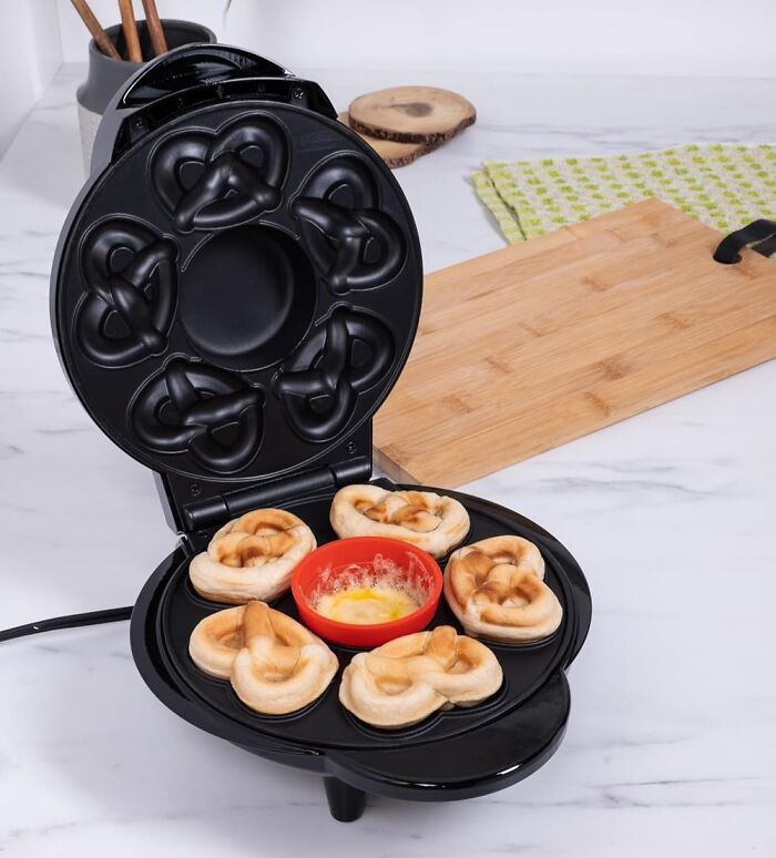 Black kitchen gadget making pretzel-shaped snacks with melted cheese dip in the center on a marble countertop.