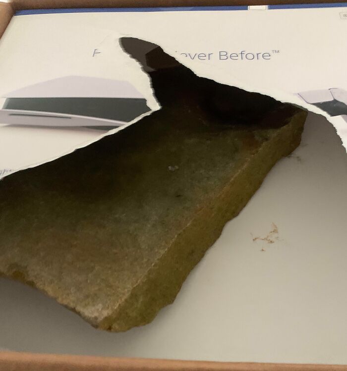 Large piece of rock or brick piercing through a cardboard box, showcasing a hilariously unlucky parenting moment.