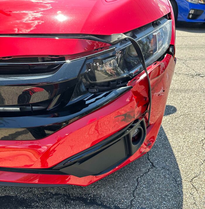 Close-up of a red car with front-end damage illustrating hilariously unlucky parents who deserve a break.
