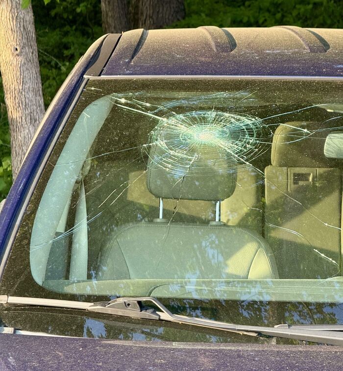 Parabrisas de coche roto con un gran impacto circular, ilustrando un día peor para padres y madres.