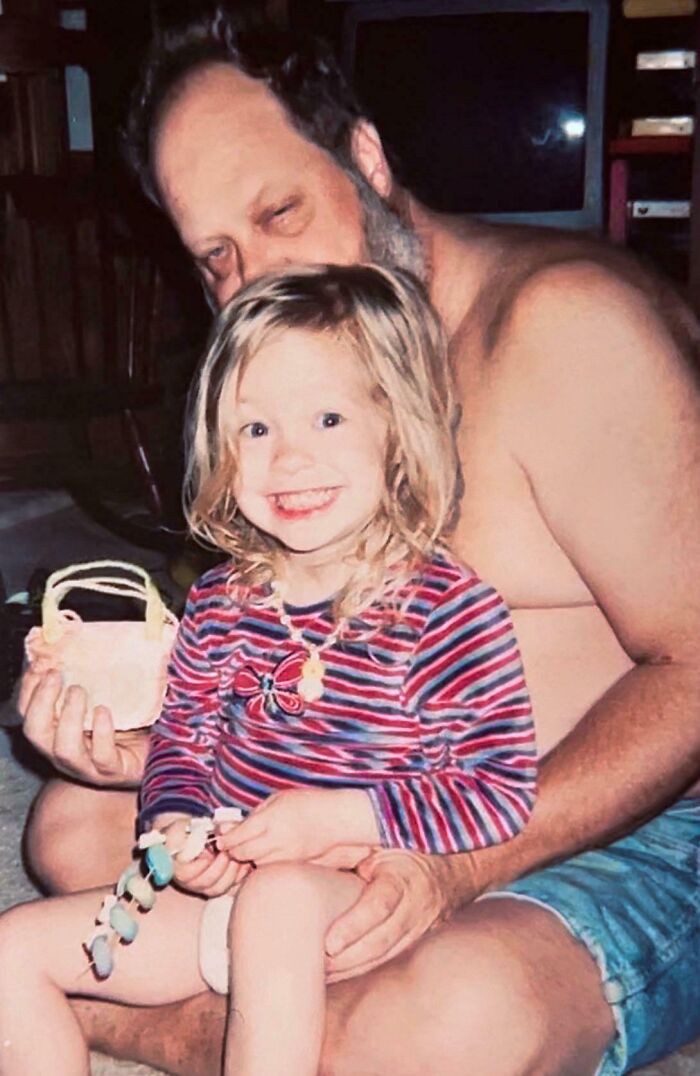Father holding a laughing toddler girl with a striped shirt, showcasing a charming moment of hilariously unlucky parents.