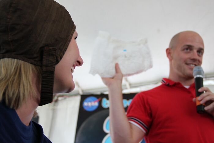 Two people at a NASA event, one holding an astronaut fact demonstration, sharing intriguing and bizarre astronaut facts.