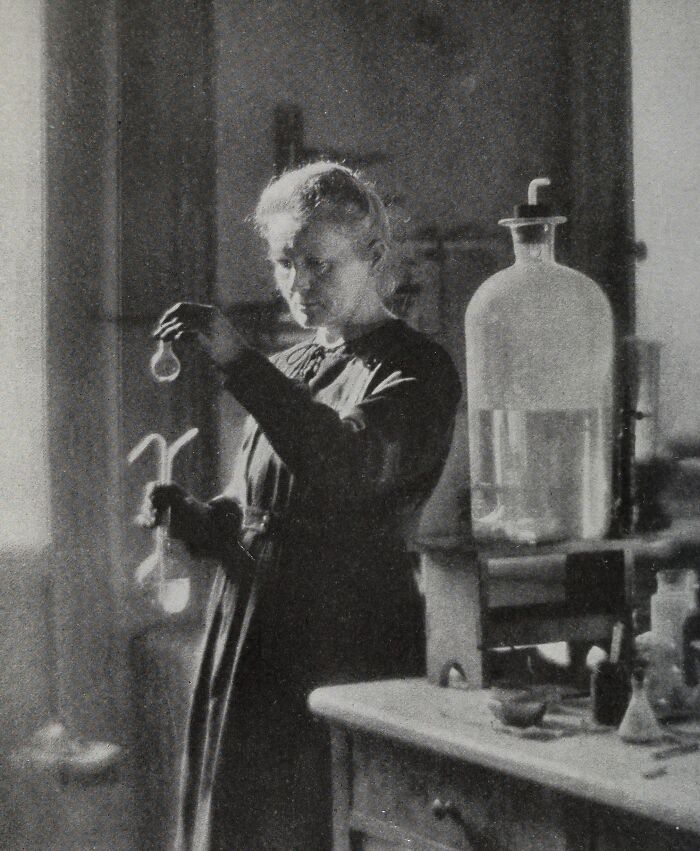Marie Curie in a vintage laboratory, carefully examining a sample while surrounded by scientific glassware and equipment.