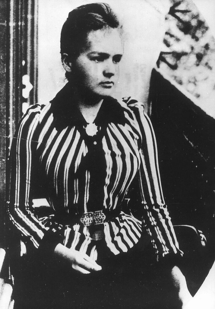 Black and white portrait of Marie Curie seated in a striped dress, reflecting on shocking facts about her life and work.