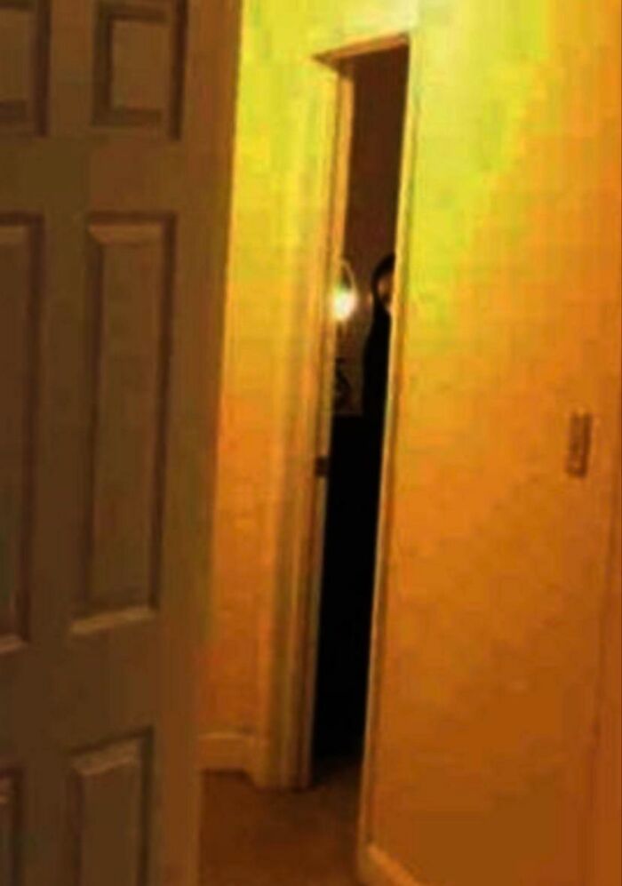 Dimly lit doorway with a shadowy figure inside, evoking chilling ghost encounters in a spooky home setting.