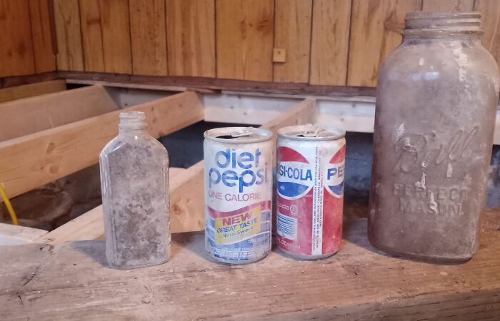 Old dusty bottles and soda cans found in walls and hidden places inside a home under renovation.