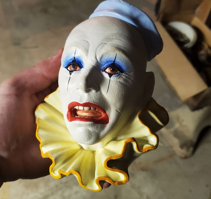 Hand holding a vintage clown head figurine, an unexpected thing found in walls and hidden places in homes.
