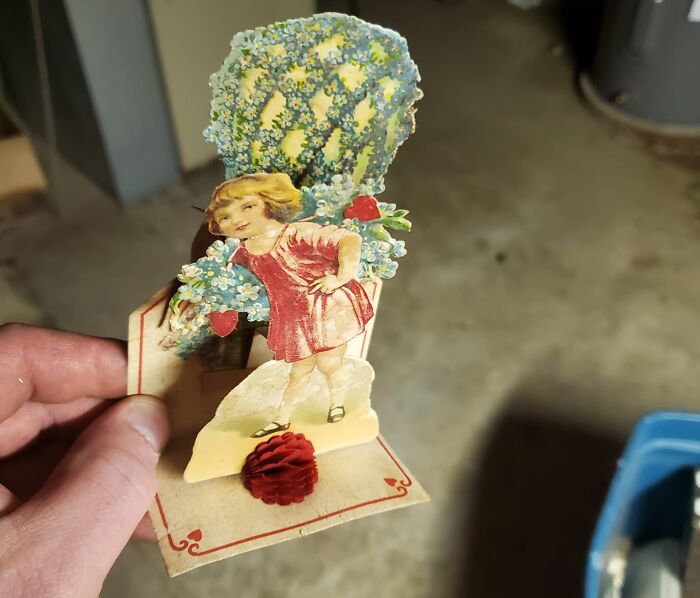 Vintage paper cutout of a girl with flowers found among unexpected things in walls and hidden places in homes.