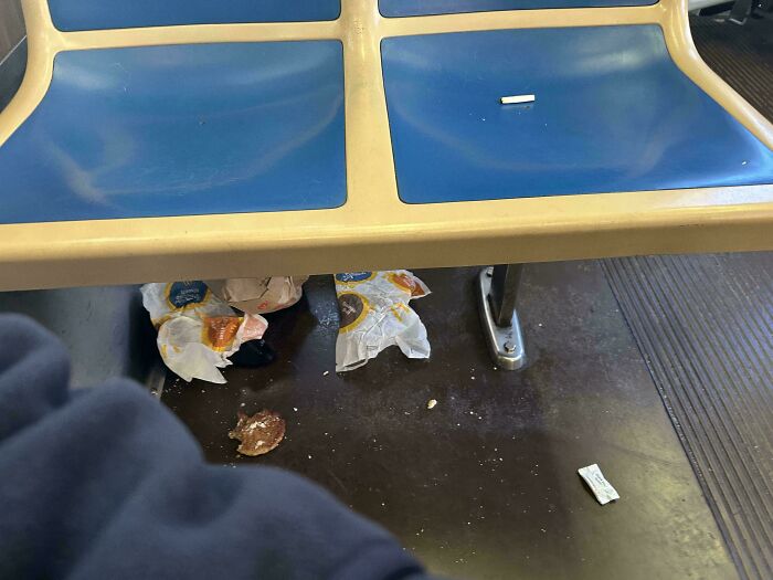 Littered floor under blue public transport seats showing messy behavior of passengers lacking consideration.