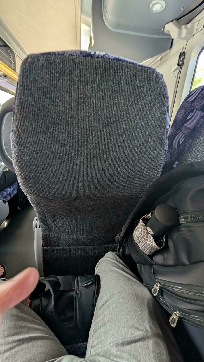 View of a public transport seat with a passenger's legs and bags blocking the aisle, illustrating bad passenger behavior.