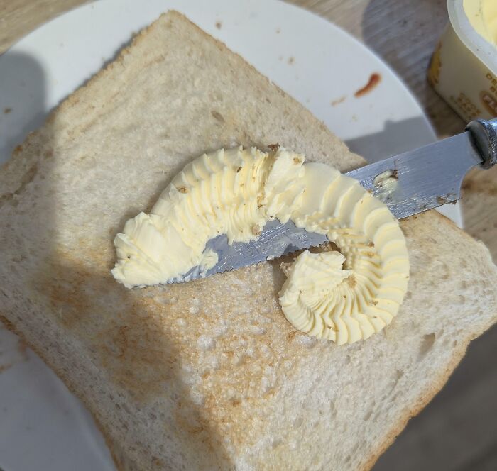 Butter curl on a knife resembling a curled caterpillar on a slice of white bread, an interesting thing requiring a double take.