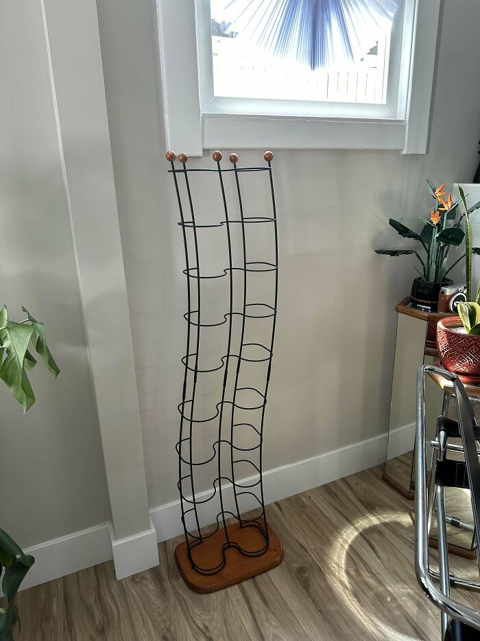 Tall narrow wire rack with wooden base and knobs, standing in a corner among houseplants and furniture mystery objects recognized online.