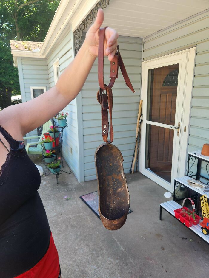 Person holding a rusty metal mystery object with leather straps outdoors in a residential patio setting.