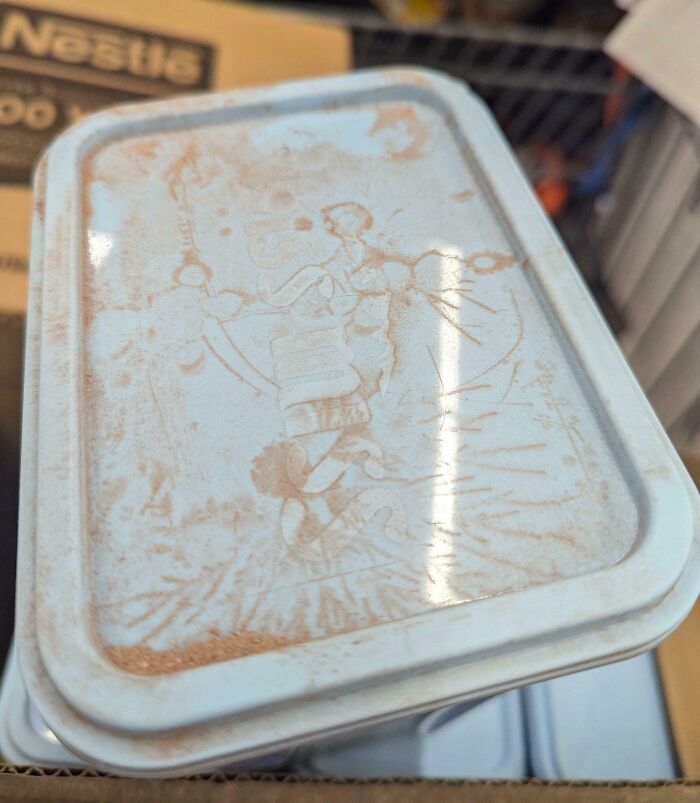 Faded image on a dusty metal lid showing a person and a child, an interesting thing requiring a double take to realize.
