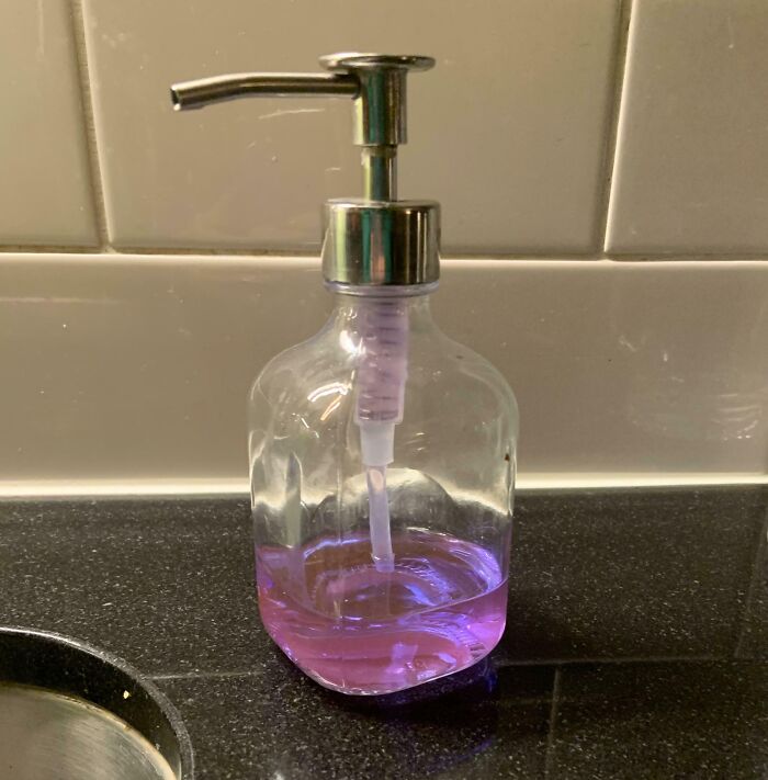 Clear soap dispenser with purple liquid on black countertop, an interesting thing requiring a double take to realize.