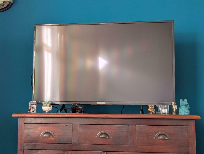 Flat screen TV reflecting a window on a wooden dresser with small figurines, an interesting thing to require a double take.