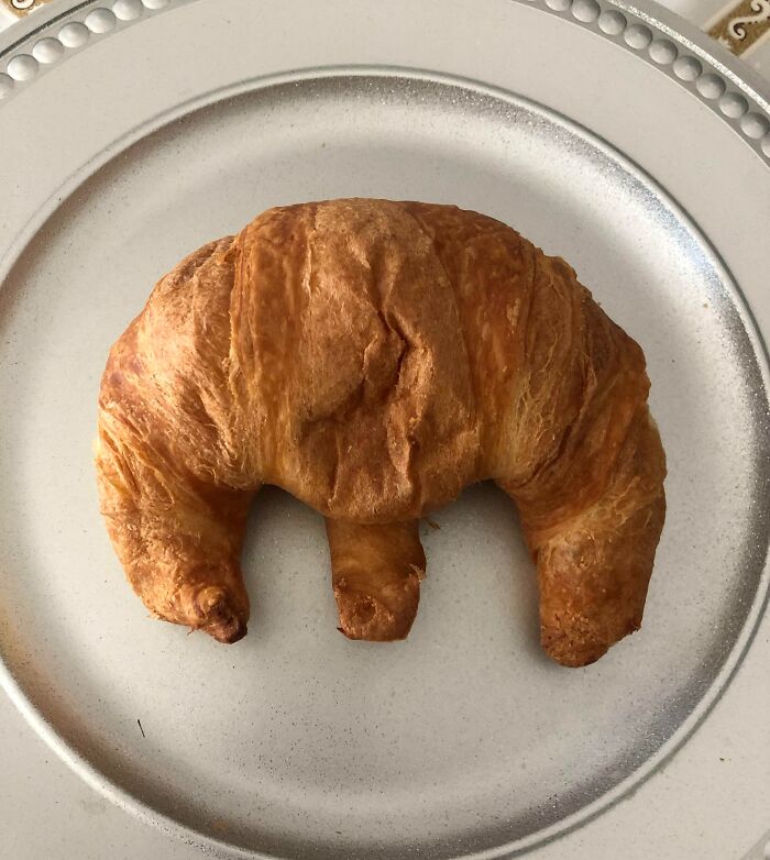 Croissant on a plate with an unusual shape that requires a double take to realize what it really is.