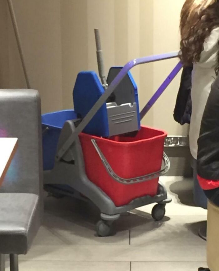 Cleaning cart with red and blue buckets parked indoors, an interesting thing that requires a double take to realize what it really is.