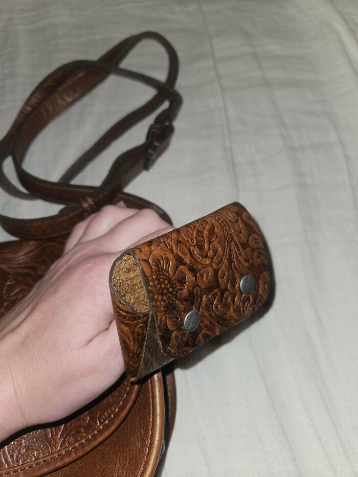 Hand holding a vintage embossed leather mystery object with straps on a fabric surface from online group recognition.