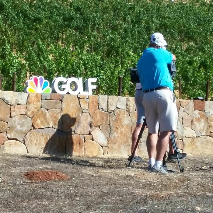 Man filming with a camera casting a cool and interesting shadow that looks like a dog silhouette on a stone wall.