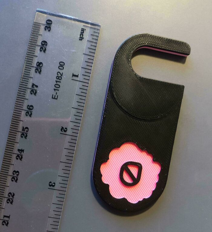 Black plastic mystery object with pink flower design next to a ruler, featured in an online group recognizing mystery objects.