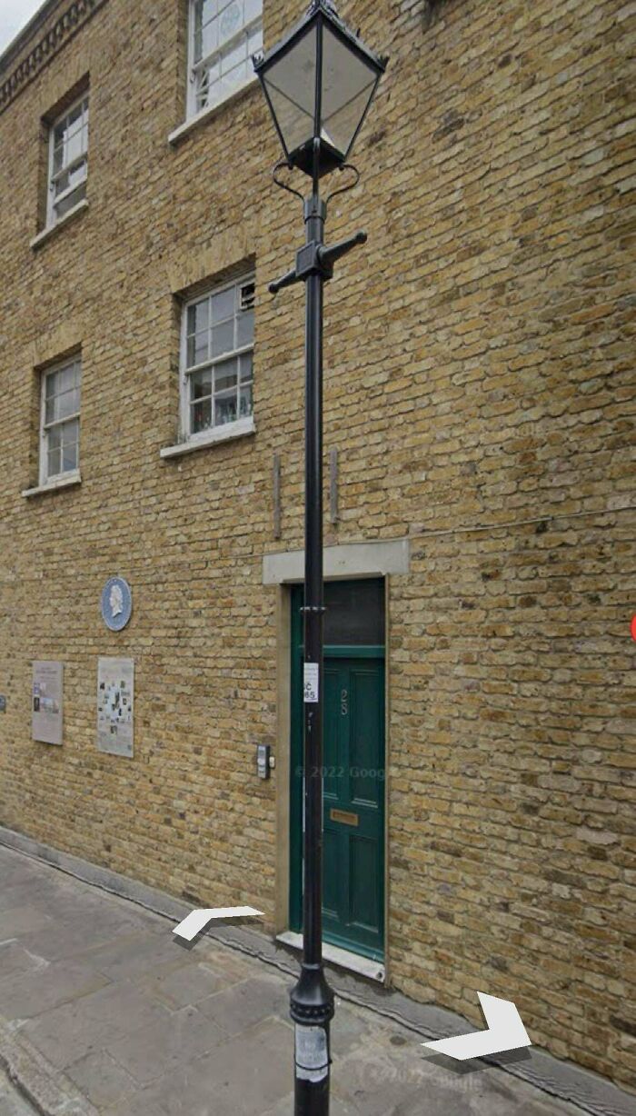 Old black street lamp on a sidewalk next to a brick building with windows and a green door in an urban setting.