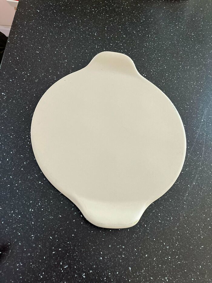 Beige flat mystery object with two small handles resting on a black speckled countertop for object recognition.