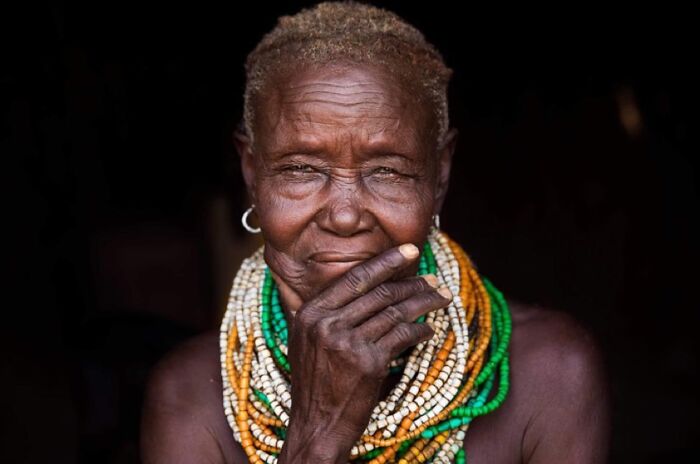 Elderly woman wearing colorful beaded necklaces, expressing wisdom and beauty with a confident gaze in natural light.