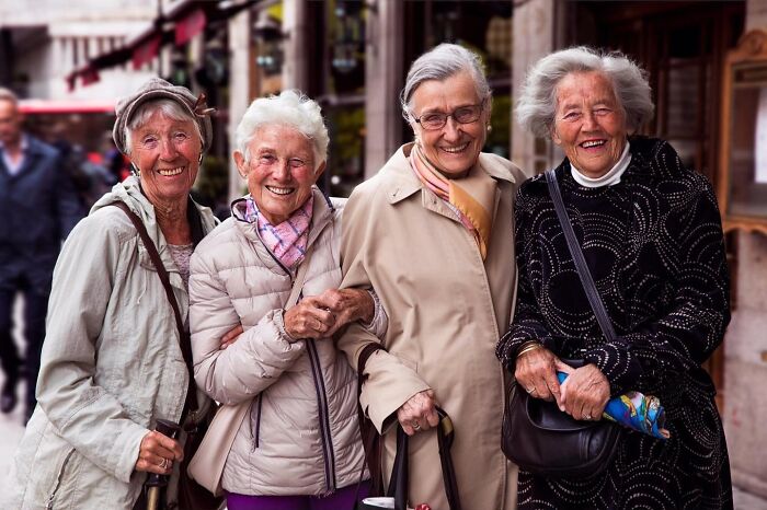 Four elderly women smiling and posing together outdoors, showcasing beauty and joy in later life.