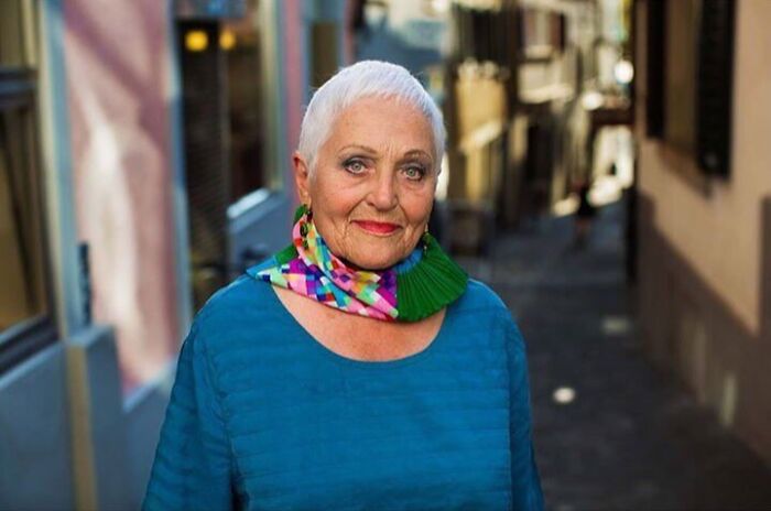 Elderly woman with short white hair wearing a colorful scarf and blue top, exemplifying beauty without expiration date.