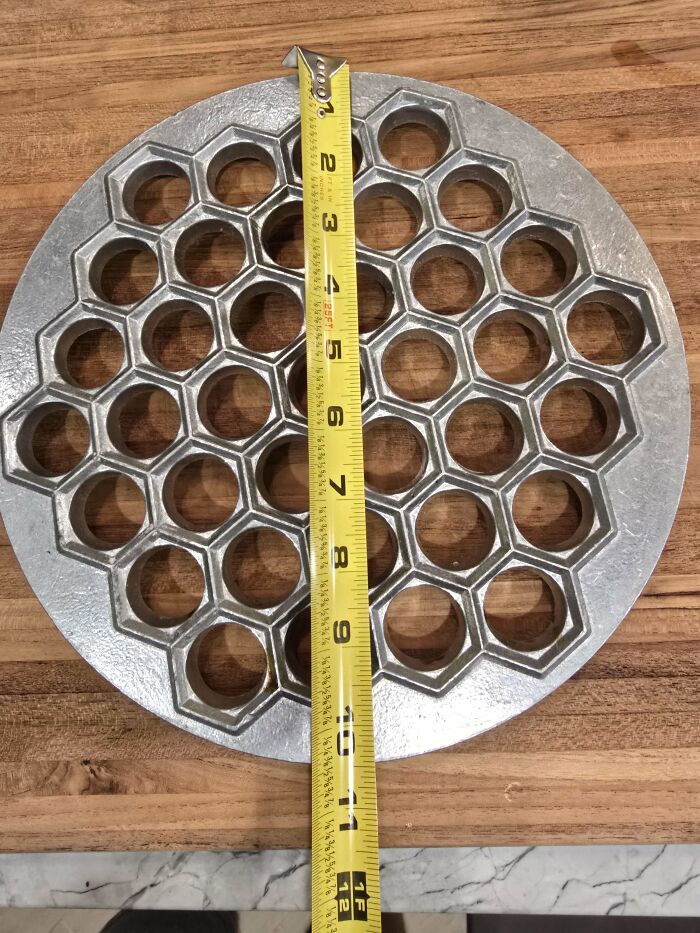 Metal round mold with hexagonal holes and a measuring tape on a wooden surface, part of mystery objects recognized online.