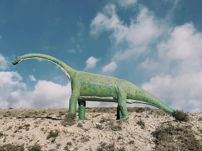 Large green dinosaur statue on a hill under blue sky, illustrating dinosaur facts and prehistoric creatures.