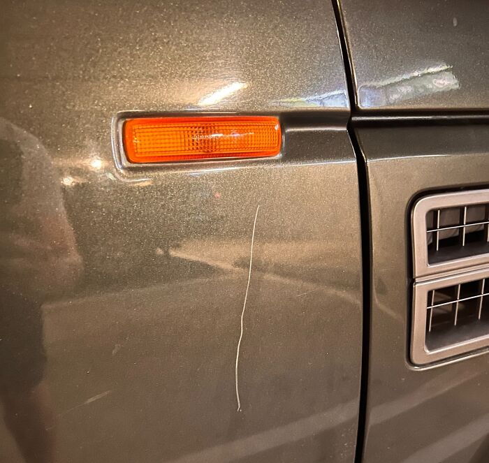 Close-up of a scratched car door with an orange side marker, showing damage from borrowed property.