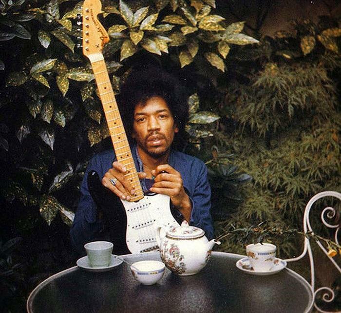 Famous person holding electric guitar outdoors at a tea table surrounded by plants in last known photos collection