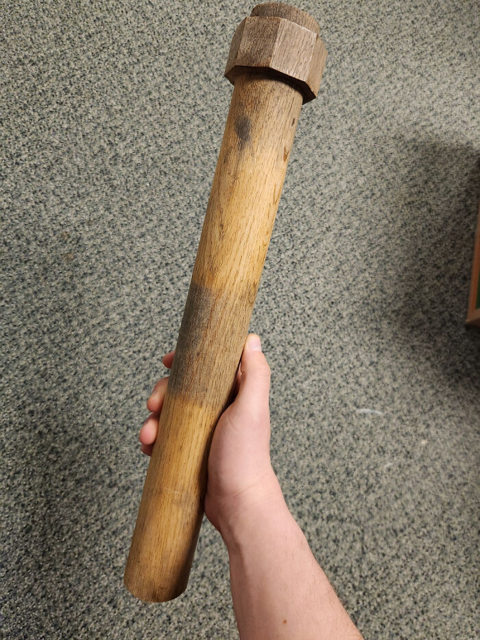Hand holding a long wooden mystery object with a hexagonal top, part of an online group recognizing mystery objects.