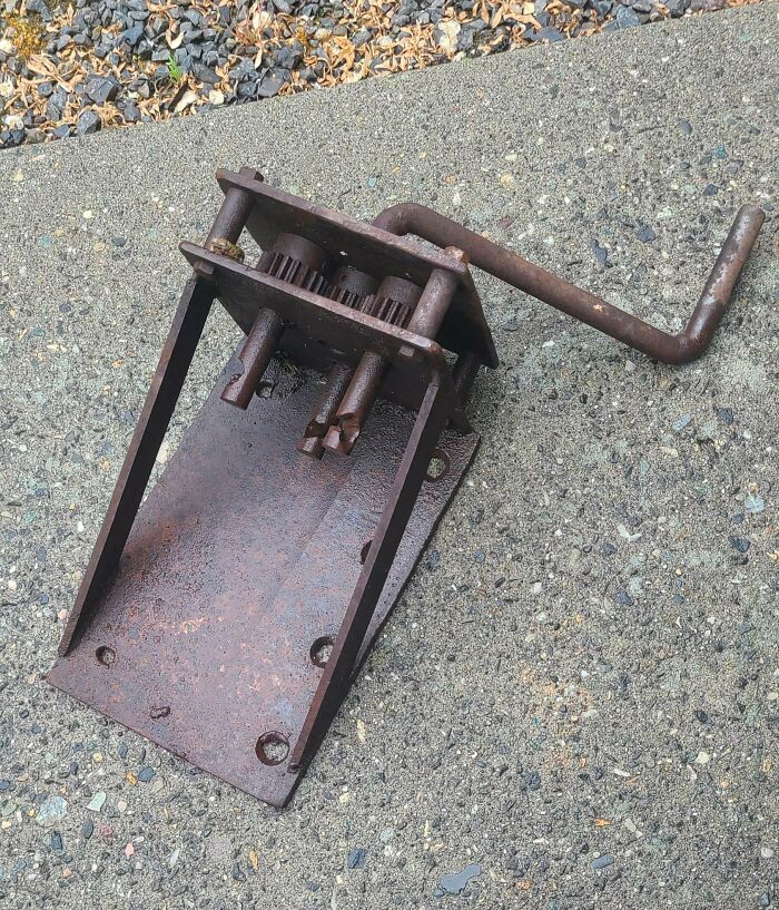 Rusty metal crank gear mechanism on pavement, an example of mystery objects online group helped recognize.