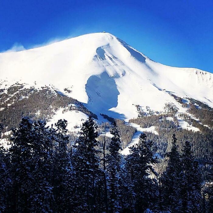 Mountain covered in snow casting a cool and interesting shadow resembling a human face under a clear blue sky.