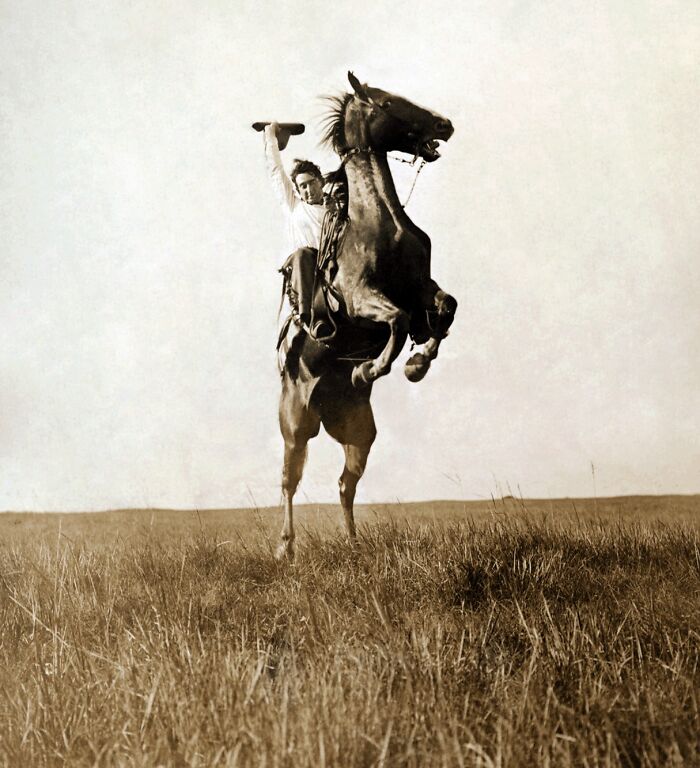 Vintage cowboy riding a rearing horse in an open field, showcasing wild west action in a classic cowboy photograph.