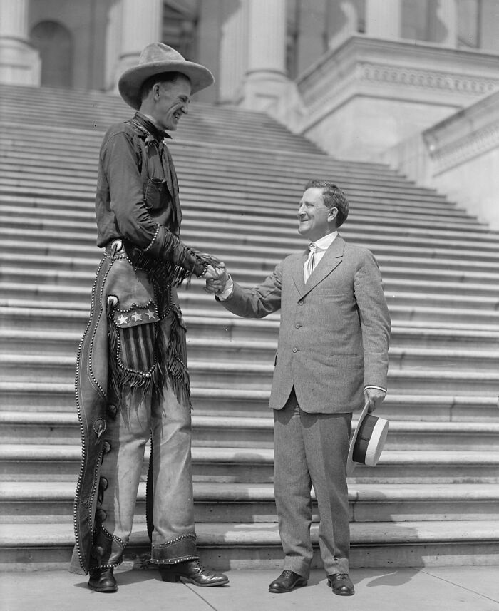 Vintage cowboy in western attire shaking hands with a man in a suit on grand building steps, vintage cowboy photograph.