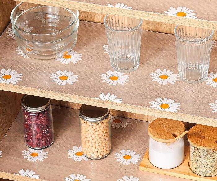 Wooden kitchen shelves decorated with daisy patterns holding glass bowls, drinking glasses, and jars of beans and spices.
